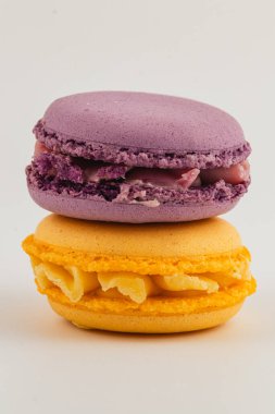 İki canlı badem kurabiyesi, biri mor diğeri sarı, üst üste güzelce istiflenmiş, pürüzsüz dokularını ve lezzetli dolgularını sergiliyorlar..