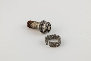 Kırık bir cıvata ve hasarlı bir tekerlek parçası düz bir yüzeyde duruyor. Bu da parçaların onarımı veya değiştirilmesi gereken olası bir mekanik arızayı gösteriyor..