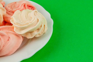 Pembe ve beyaz kremalı kurabiyelerden oluşan bir seçim canlı yeşil bir arkaplanda beyaz bir tabakta oturmakta, hassas dokularını ve girdap tasarımlarını sergilemektedirler..