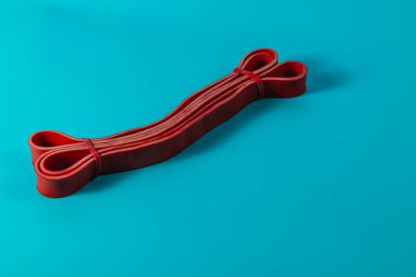 Kırmızı elastik bir bant, parlak mavi bir zemin üzerinde dinlenerek, çeşitli kullanımlar için canlı rengini ve esnekliğini gösteren döngülerle güzelce sarmalanır..