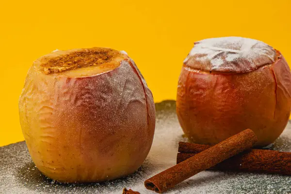 Lezzetli fırınlanmış elmalar tatlı tarçın ve şekerle doldurulur, sıcak bir ikram oluşturur. Parlak sarı arka plan bu yemeğin sıcak havasını arttırır..