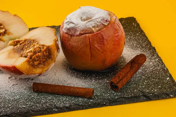 Bu nefis pişmiş elmalı tatlı, parlak sarı bir zemin üzerinde koyu bir levha üzerinde pudra şekerle tozlanmış tarçın dolgusu içerir..