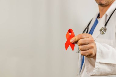 Bir tıp uzmanı, HIV 'den etkilenenlerin AIDS farkındalığı ve desteklenmesinin yaygın bir sembolü olan kırmızı bir kurdele sergileyen klinik bir ortamda duruyor. Konferansta sağlık savunucuları.