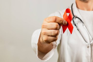 Sağlık çalışanı tıbbi bir ortamda HIV / AIDS hakkında farkındalığı artırmak için kırmızı kurdele tutuyor. Görüntü, eğitimin ve etkilenen bireyler için desteğin önemini vurguluyor.