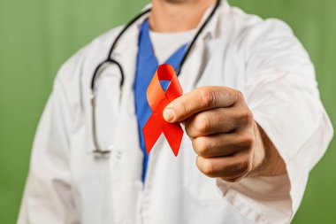 Beyaz önlüklü ve steteskoplu bir tıp uzmanı, sağlık sorunlarına verilen desteği ve farkındalığı belirten kırmızı bir kurdele sergiliyor. Kurulum sağlık eğitiminin savunuculuğunu vurguluyor.
