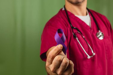 Önlüklü bir sağlık görevlisi farkındalığı sembolize eden mor bir kurdele sunar. Kurulum bir klinik ve sağlıkla ilgili bir şeyi desteklemeye odaklanıyor..