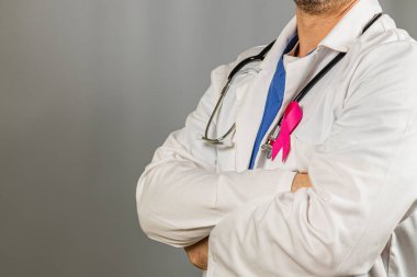 Bir sağlık uzmanı, göğüs kanseri farkındalığını desteklemek ve sağlık konuşmalarını teşvik etmek için kollarını kavuşturup laboratuvar önlüklerinde pembe bir kurdele taşıyor..