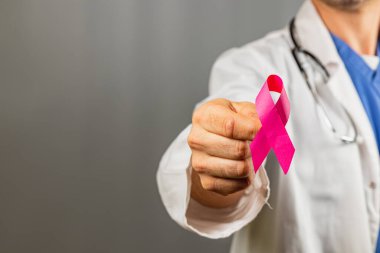 Bir tıp uzmanı, sağlık ortamında kanser farkındalığını sembolize eden pembe bir kurdele tutuyor. Jest, kanser araştırma girişimlerine farkındalık ve desteği artırmayı amaçlıyor.