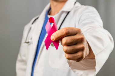 Bir sağlık uzmanı klinikte elinde canlı pembe bir kurdele ile duruyor. Bu, farkındalık ayı boyunca göğüs kanserine verilen desteği ve farkındalığı sembolize eder..