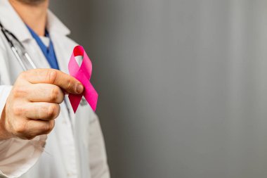 Bir sağlık uzmanı meme kanseri farkındalığını sembolize eden pembe bir kurdele taşıyor. Ortam, erken teşhis ve destekle ilgili sağlık girişimlerini ve hasta eğitimini destekleyen bir kliniktir..