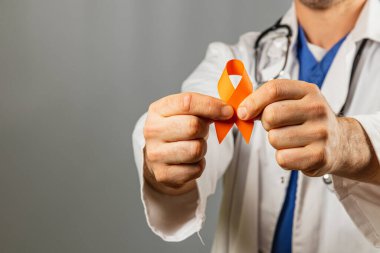 Beyaz önlüklü bir sağlık çalışanı, klinik ortamda sağlık sorunlarına verilen desteği sembolize eden bir turuncu farkındalık kurdelesi sergiliyor. Bireyler farkındalığa bağlılıklarını gösterirler..
