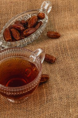Zengin çayla dolu güzel bir cam bardak dekoratif bir kristal tabağın yanına yerleştirilir. İçinde birkaç tatlı hurma vardır. Hepsi desenli bir çuval bezi kumaşa dizilmiştir..