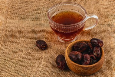 Sıcak bir fincan kahve, bir çuval bezi yüzeyinde bir kase tatlı hurma ile eşleştirilir. Rahatlatıcı bir öğleden sonrası için mükemmel bir kırsal titreşim yaratır..