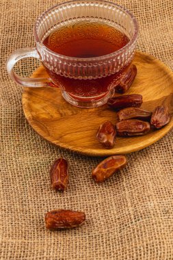 Cam bardakta, lezzetli taze hurma dolu ahşap bir tabağın yanında dumanı tüten kahverengi çay bulunur. Hepsi de kırsal bir arka plana yerleştirilir ve davetkar bir atmosfer yaratır..