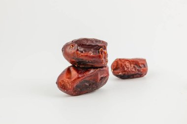 Kurumuş üç tarih beyaz bir yüzeyde, zengin, koyu renkleri ve pürüzsüz dokuları ile sergilenir. Odak, onların doğal tatlılıklarına ve çekiciliğine vurgu yapıyor.