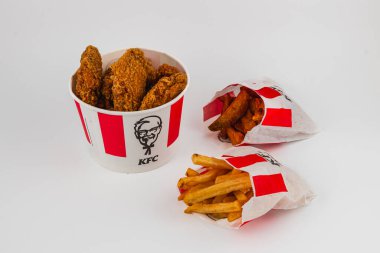 Lviv Ukrayna 05.21.25. Kızarmış tavuk dolu bir kova, iki paket altın patates ile çevrili. Tadını çıkarmaya hazır, cezbedici bir fast-food ziyafeti hazırlıyor..