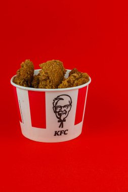 Lviv Ukrayna 05.21.25 Kıtır kıtır kızarmış tavukla dolu bir kova canlı kırmızı bir arkaplanda oturur, altın kahverengi dokusunu gözler önüne serer ve yiyeceklerin büyüleyici sunumunu yapar..