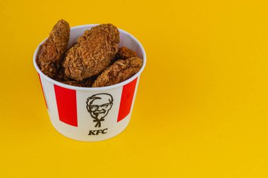 Lviv Ukrayna 05.21.25 Bir kova kızarmış tavuk parlak sarı arka planda sergilenir. Kova lezzetli tavuk parçalarını gösterirken tanınabilir bir logo içeriyor..