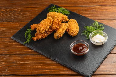 Kızarmış tavuk parçaları kaykay tahtasında sunulur. Barbekü sosu ve taze otlarla süslenmiş kremalı sos, sağlıklı bir yemek için mükemmel olur..