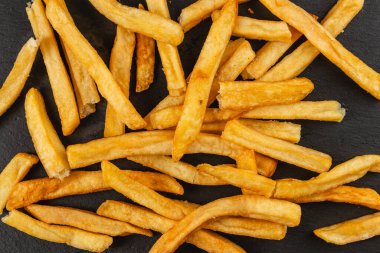 Freshly cooked golden fries are arranged haphazardly on a dark surface, showcasing their crispy texture and appetizing appeal during a casual meal.