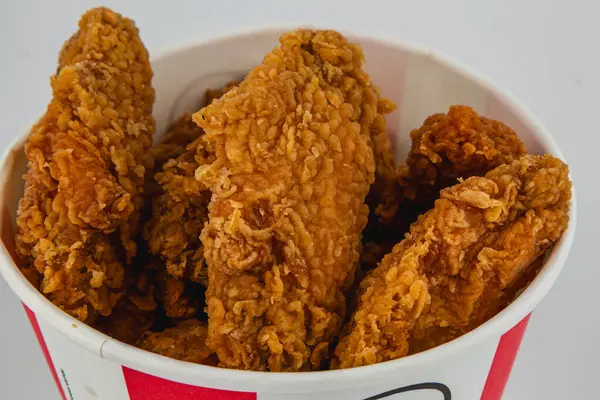 Lviv Ukrayna 05.21.25 altın sarısı kızarmış tavuk şeritleri kırmızı ve beyaz kağıt bir kabın içinde üst üste dizilir ve çıtır çıtır dokuları ve davetkar görünüşleri sergilenir..