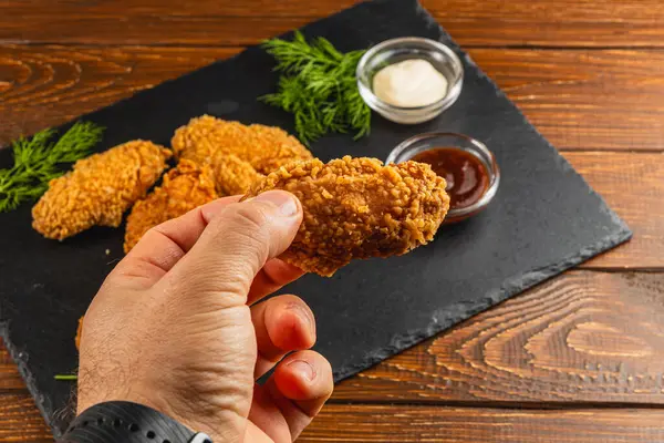 Bir el kızarmış tavuk kanadı tutar. Etrafında birkaç kanat daha vardır. Küçük kaselere soslar batırılarak tamamlanır..