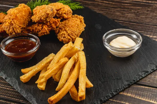 Sulu kızarmış tavuk parçaları yanında altın patates kızartmaları ve cam kâseler dolusu barbekü sosu ve kremalı sos, lezzetli bir yemek deneyimi vaat ediyor..