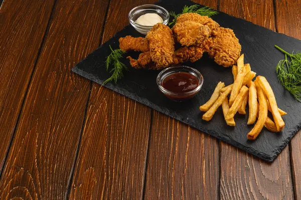 Kızarmış tavuk, yanında altın kızartma ve küçük bir tabak sosla servis edilir. Lezzetli ve cezbedici bir yemek sunumu yaratır..