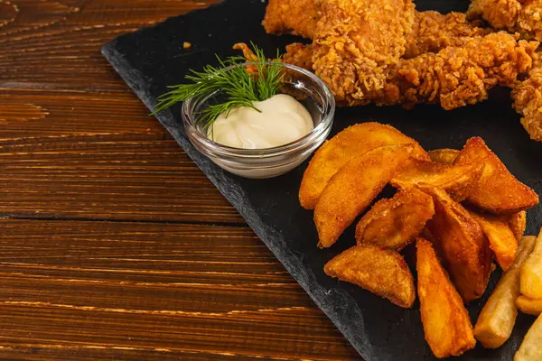 Tabakta kızarmış tavuk parçaları ve yanında koyu ahşap bir masa üzerine kurulmuş küçük bir kase kremalı sos var..