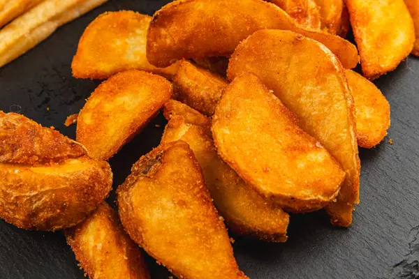 Altın sarısı patates kamaları, çıtır çıtır dokularını gösteren siyah bir tabakta sıralanır. Batırmak için mükemmel. İdeal bir aperatif ya da aperatif olurlar..