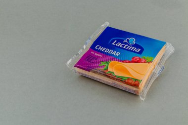 Lviv Ukrayna 05.22.25 Cheddar peyniri gri bir yüzey üzerinde renkli markalaşma ile güzelce paketlenmiştir, çekici dokusunu ve çeşitli yemeklerde kullanılmaya hazır pürüzsüz dilimlerini göstermektedir..