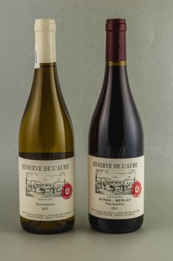 İçinde 2023 yılından kalma Rezerv de L 'Aube ve kırmızı Syrah-Merlot etiketli beyaz bir şarap bulunan iki şişe yan yana oturur. İkisi de kaliteli Fransız şaraplarının altını çiziyor..