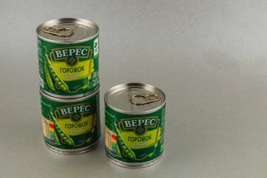 Lviv Ukrayna 05.22.25 Üç kutu yeşil bezelye nötr gri bir zemin üzerinde birbirine yakın dizilmiştir. Etiketlerde kolay açılan sekmelerle canlı yeşil tasarımlar yer alıyor.