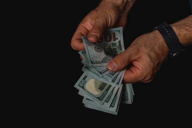 Ellerinde bir yığın yüz dolarlık banknot var. Düşük ışıklı bir ortamda dikkatle sayıyorlar. Gizlilik ve finansal işlem hissini aktarıyorlar..