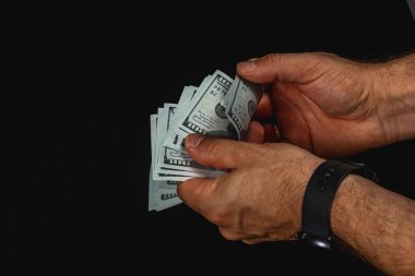 İki elini dikkatlice ayır ve birkaç yüz dolarlık banknotları karanlık bir arkaplan karşısında say, para biriminin dokusunu ve detaylarını vurgula.