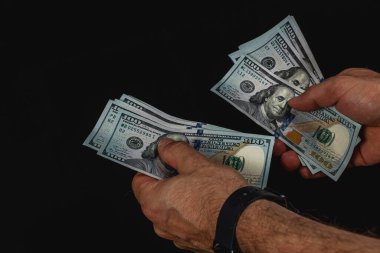 İki el düzenli olarak düşük ışık altında 100 dolarlık banknotları sayar, paranın dokusunu ve detaylarını vurgular, odaklanmış bir atmosfer yaratır..