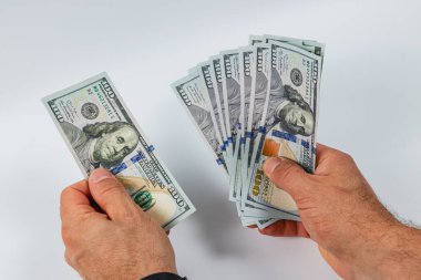 Bir kişi titizlikle sayarken bir yığın 100 dolarlık banknot tutuyor. Ayarlar nötr renkli bir tablo gibi görünüyor, dikkat dağıtıcı bir şey yok..