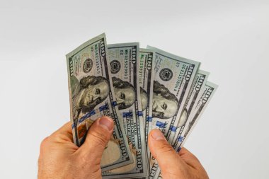 İki el, birkaç yüz dolarlık banknotları kavrayıp para biriminin detaylarını bembeyaz bir arka planda sergiliyor. Para belirgin bir şekilde sergileniyor.