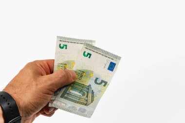 Bir el, iki adet beş avroluk banknotu düz beyaz bir arkaplana dayayarak, para birimi tasarımı ve paydasını parlak ışık altında sergiliyor.