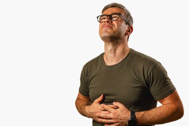 Bir adam gözleri kapalı durur, karnını tutarken rahatsızlığını ifade eder. Bir sıkıntı ya da acı içinde gibi görünüyor..