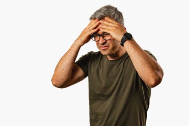 Elleri başının üstünde duran bir adam hayal kırıklığı belirtileri gösterir. Gri saçları ve gözlükleri var. Sade bir ortamda sıkıntılı görünüyor..