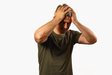 Elleri başının üstünde duran bir adam stres ve hayal kırıklığı belirtileri gösterir. Ayar, duygusal mücadelesini vurgulayan tarafsız bir arkaplan içeriyor..