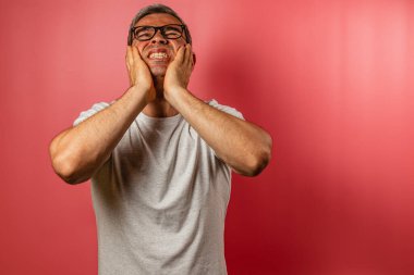 Gri tişörtlü bir adam yüzünü hüsran içinde tutuyor, gözle görülür sıkıntı belirtileri gösteriyor. Parlak pembe arka plan duygularına şaşırtıcı bir zıtlık katıyor..