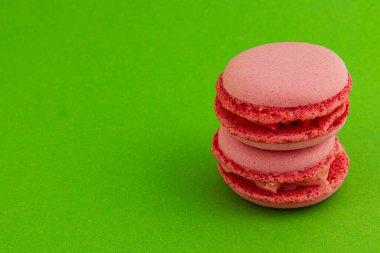 İki pembe badem kurabiyesi bir araya toplanmış, pürüzsüz dokularını ve kremsi dolgularını canlı yeşil bir zemine karşı sergiliyorlar. Tatlı severler için mükemmel..