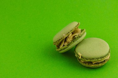 Açık yeşil kremayla doldurulmuş iki yeşil badem kurabiyesi parlak yeşil bir arka planda oturur, desenli yüzeylerini sergilerler ve renkli kontrastları cezbeder..