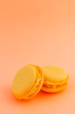 Kremayla dolu iki canlı sarı badem kurabiyesi yumuşak şeftali arka planına karşı yan yana oturur, hoşgörü ve zevki davet eder..