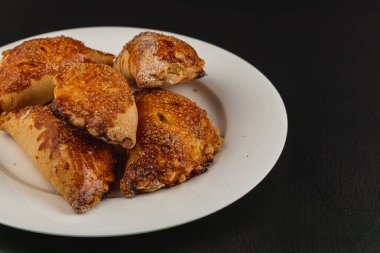 Bir tabakta bir kaç altın-kahverengi balkabağı pastası var, çıtır çıtır ve şekerli bluzlarını sergiliyorlar. Çelişkili koyu arka plan, ikramların sıcak tonlarını arttırır..