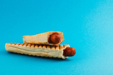 İki sosisli sandviç yaratıcı bir şekilde kızartılmış ekmeklerin içine yerleştirilir, canlı mavi bir arka plana karşı dizilir, klasik bir aperatifte yenilikçi bir kıvrım sergilerler..