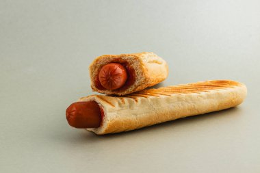 Kızarmış ekmeğin üzerine iki sosisli, minimalist bir stil sergiliyorlar. Yemekler düz bir arkaplana karşı düzgünce dizilmiş, renkleri ve dokuları vurgulanıyor..