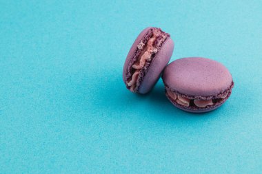 Kremalı çikolatayla dolu iki mor badem kurabiyesi açık mavi bir zemine oturup narin dokusunu ve çekici rengini gözler önüne seriyor..